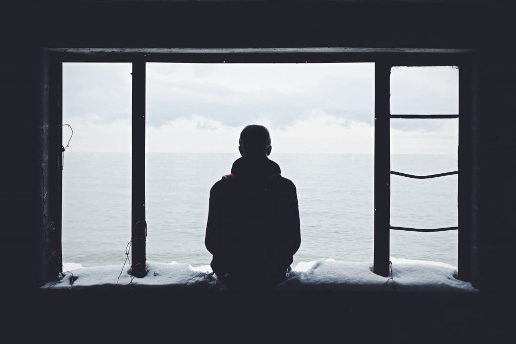 silhouette of person sitting under snowy dock looking out at the water