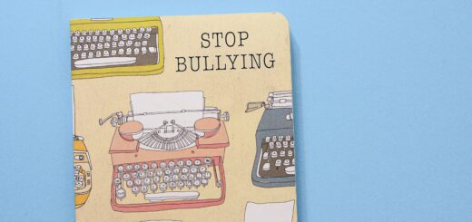 A blue background; an image of a tan writing journal with images of typewriters on the cover in various colors; the cover of the journal has the words "STOP BULLYING"