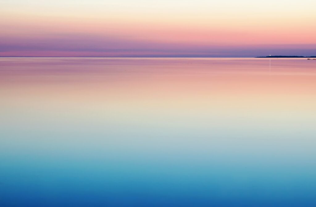 This is a picture of a body of water at twilight with blue and pink hues. There is also a lighthouse in the far distance. 