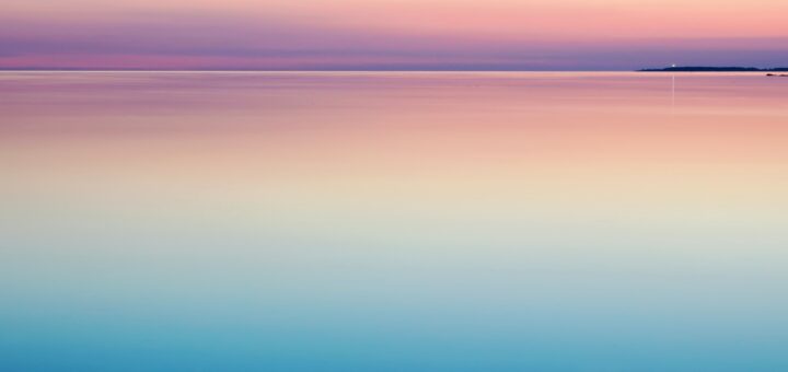 This is a picture of a body of water at twilight with blue and pink hues. There is also a lighthouse in the far distance.