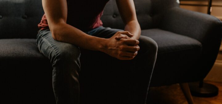 this is a picture of a person sitting on a couch with his/her hands crossed. You cannot see the person's face.
