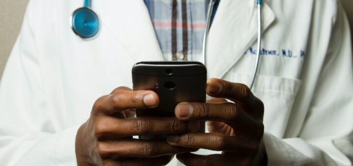picture of hands holding a phone; person is wearing a lab coat and is a doctor