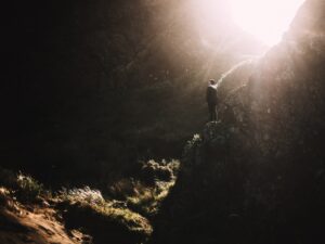 This is a picture of a cave and there is a person standing in a cave and at the top of the frame the sun is coming down, shining on the person