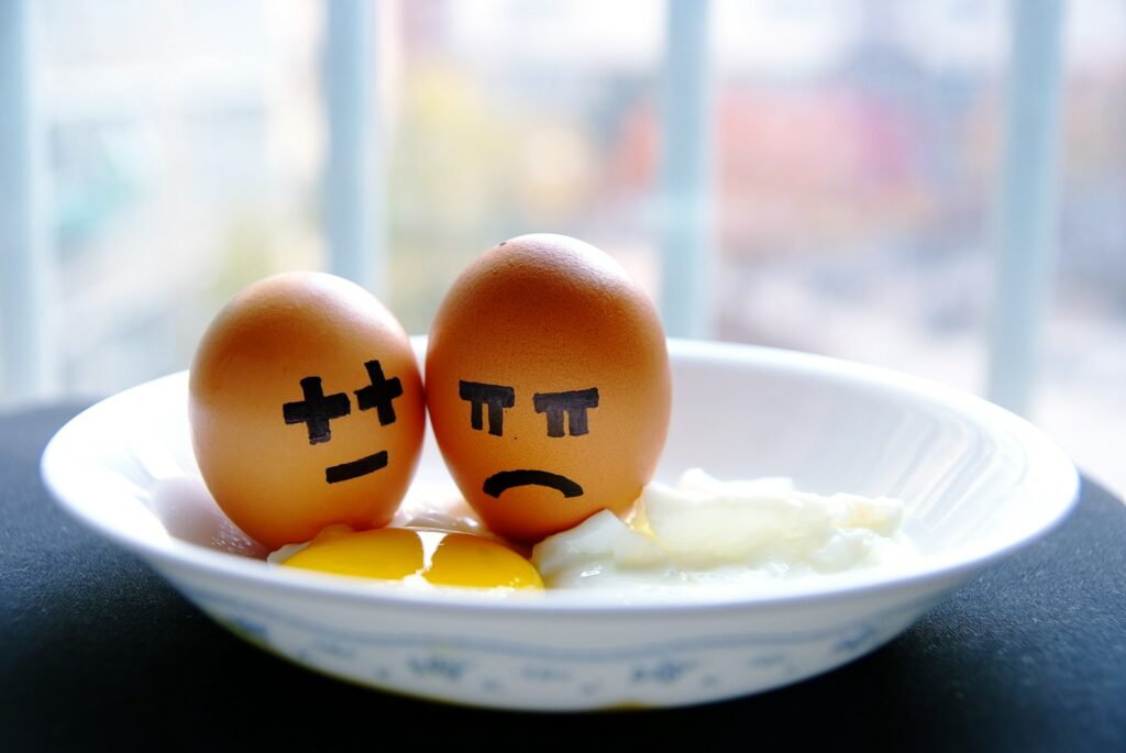 This is a photo of two eggs with faces drawn on them, and one face is unhappy. The eggs are inside of a plate which is on a table and the background is blurred-out.