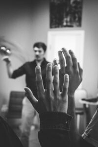 This is a black and white photo of a classroom with the instructor blurred in the background and two raised hands in clear focus.