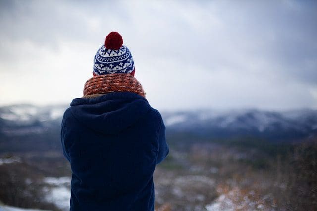 person standing on a hill. blurred in the background is a mountain. Person is facing away from the camera wearing winter clothing.